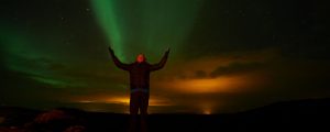 Ein Mann steht in der Nacht und aus seinen hochgehaltenen Händen sieht es so aus, als strömten die Polarlichter aus ihm.