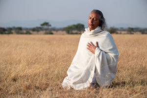 In völliger Hingabe meditierender Mann in der Serengeti umhüllt mit weißem Schal