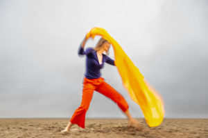 hingebende und tanzende Frau am Strand mit gelben Tuch in Bewegung